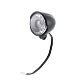 The Frontlicht is a black, round bicycle headlight with a clear lens, attached wiring, and a white connector, shown on a white background.